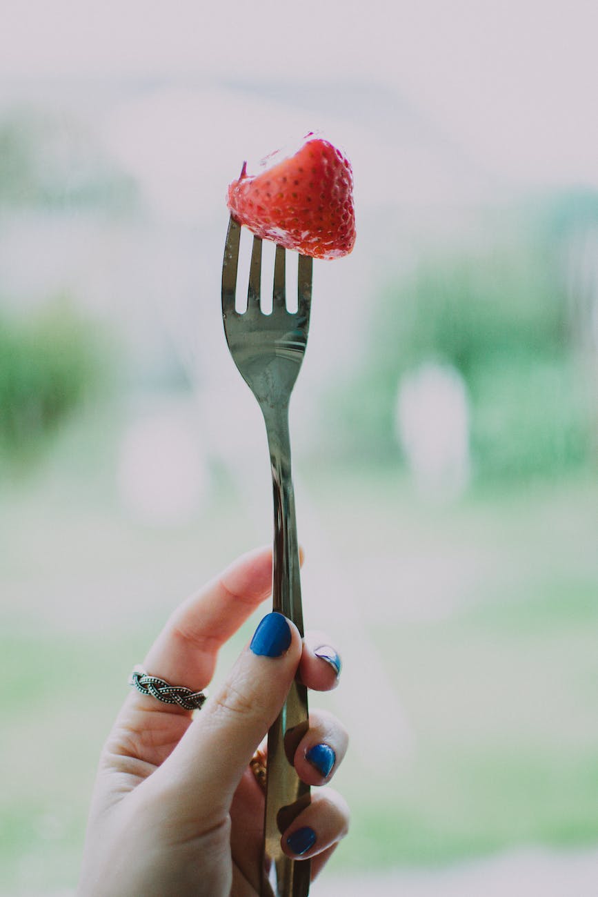 person holding gray steel fork with strawberry